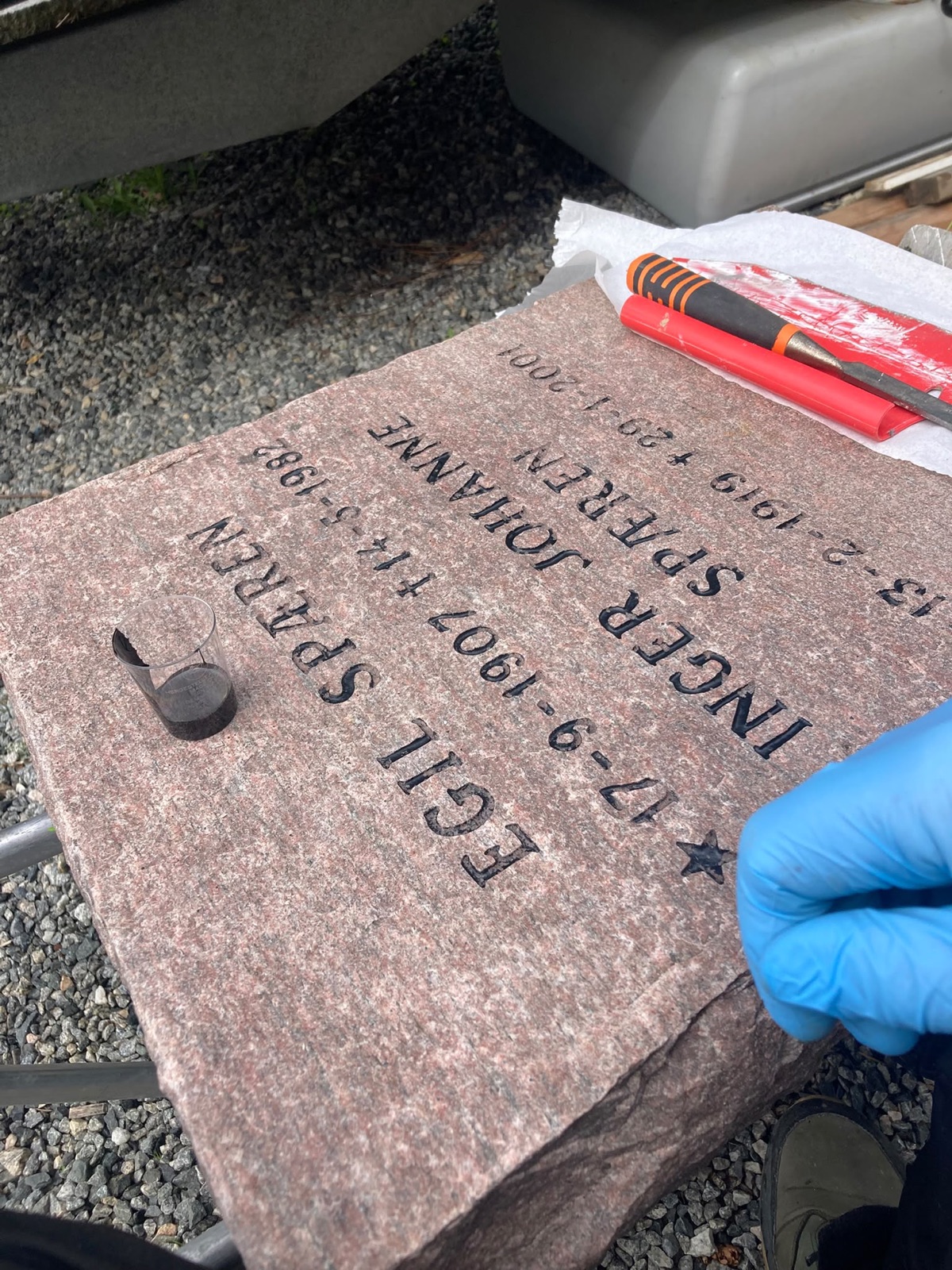 Den rensede steinen ligger flatt på stativ mens bokstavene males opp for hånd, med malingskopp og verktøy ved siden av.