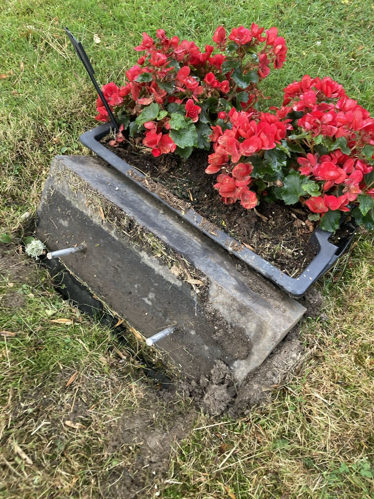 Sokkelen etter at steinen er løftet av, med festepinnene synlige og plantekassen bak.